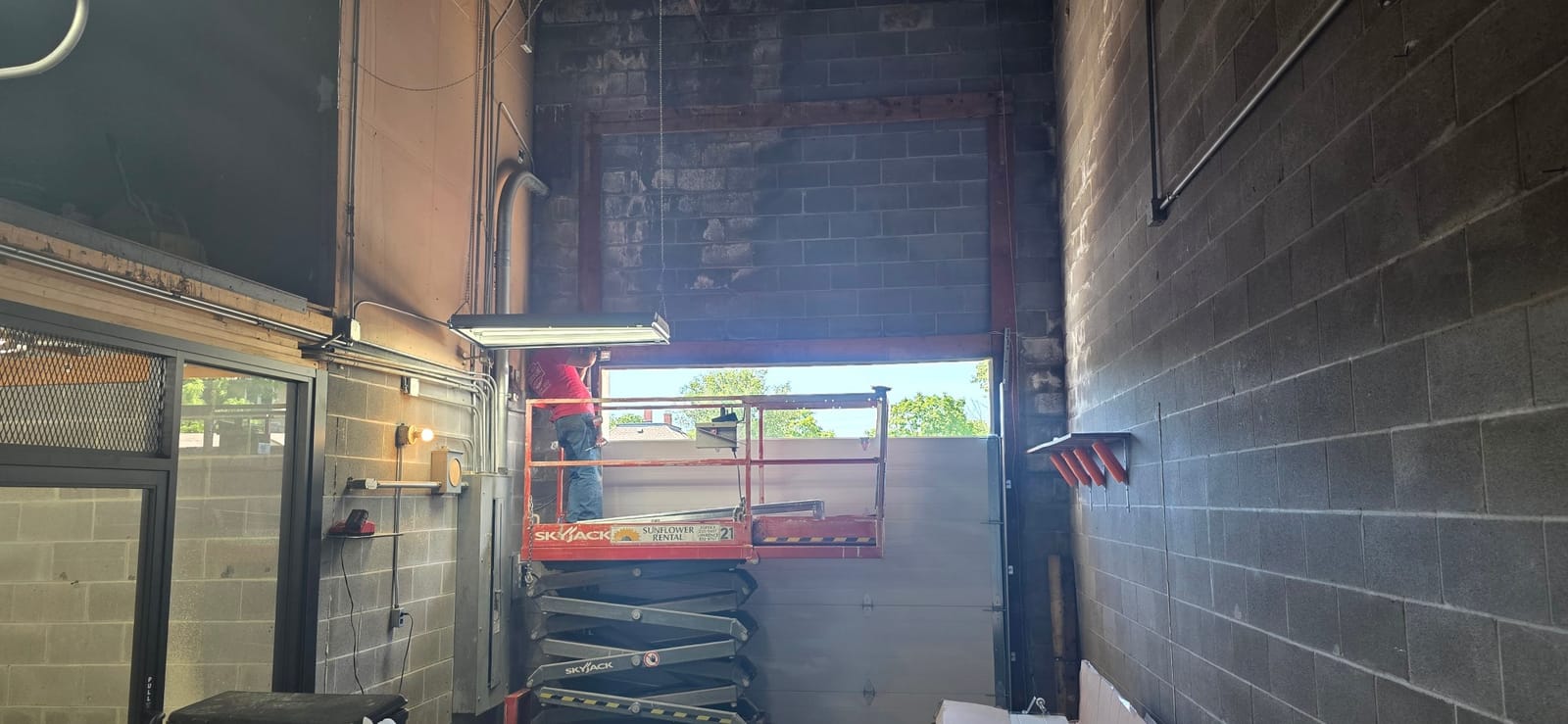 Technician on a scissor lift installing sections in a tall cinder-block commercial door opening in Independence, MO