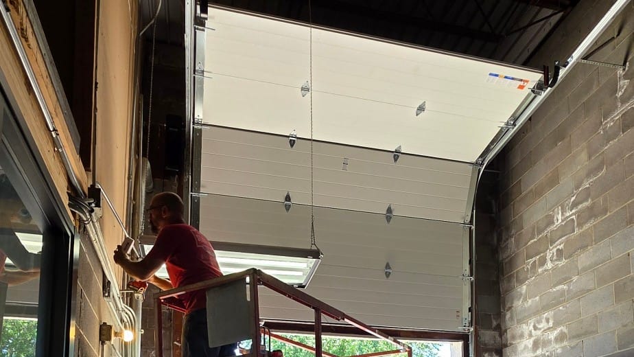 Technician on a scissor lift installing an insulated sectional door in a commercial bay in Independence, MO